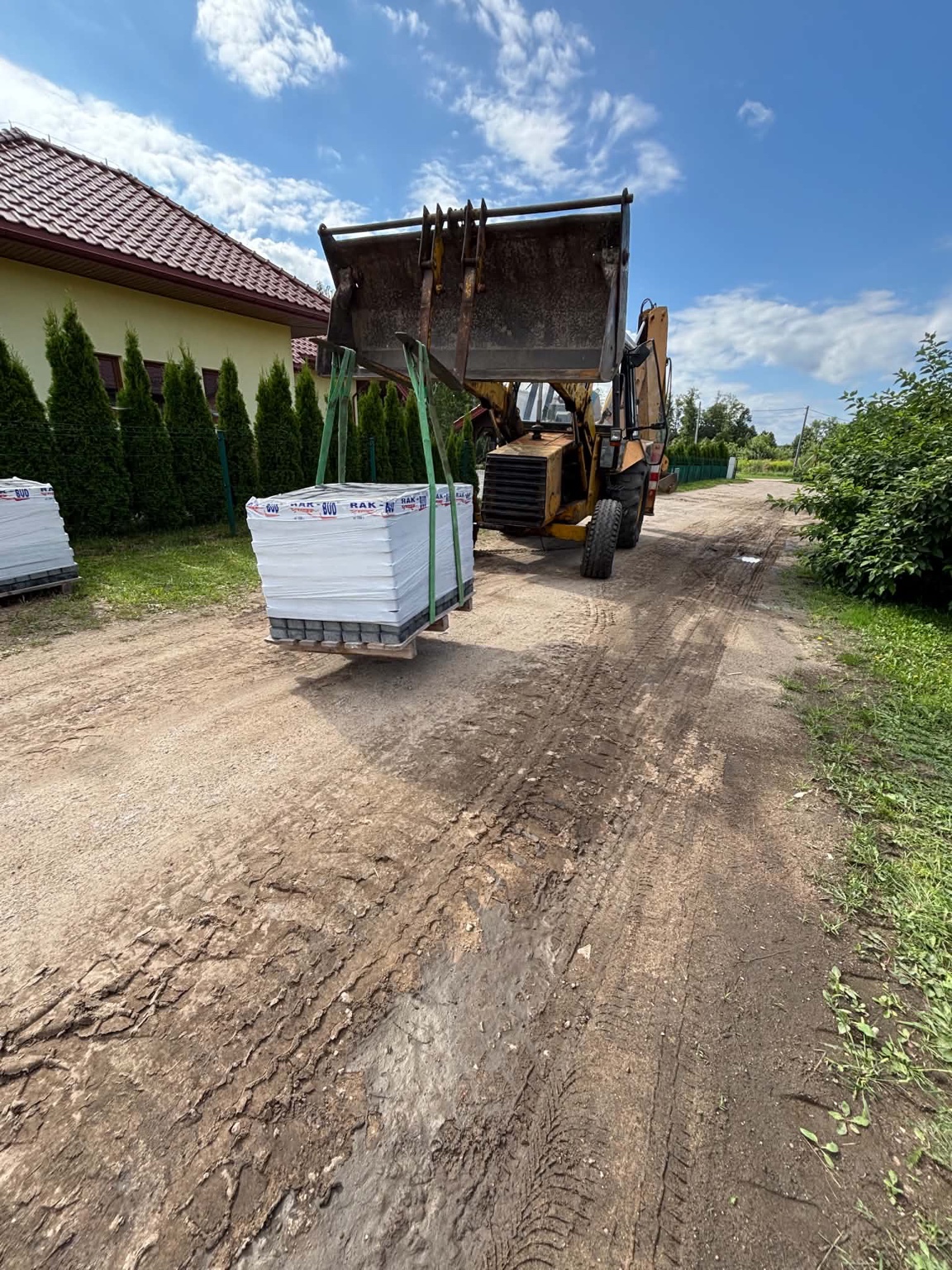 Koparko-ładowarka przenosząca paletę materiałów budowlanych